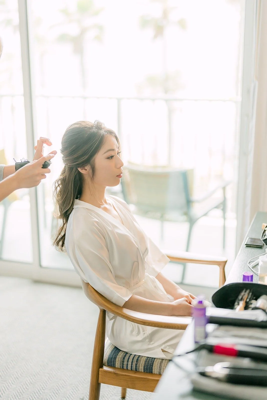Angela having her hair styled in a white robe by the window at The Seabird