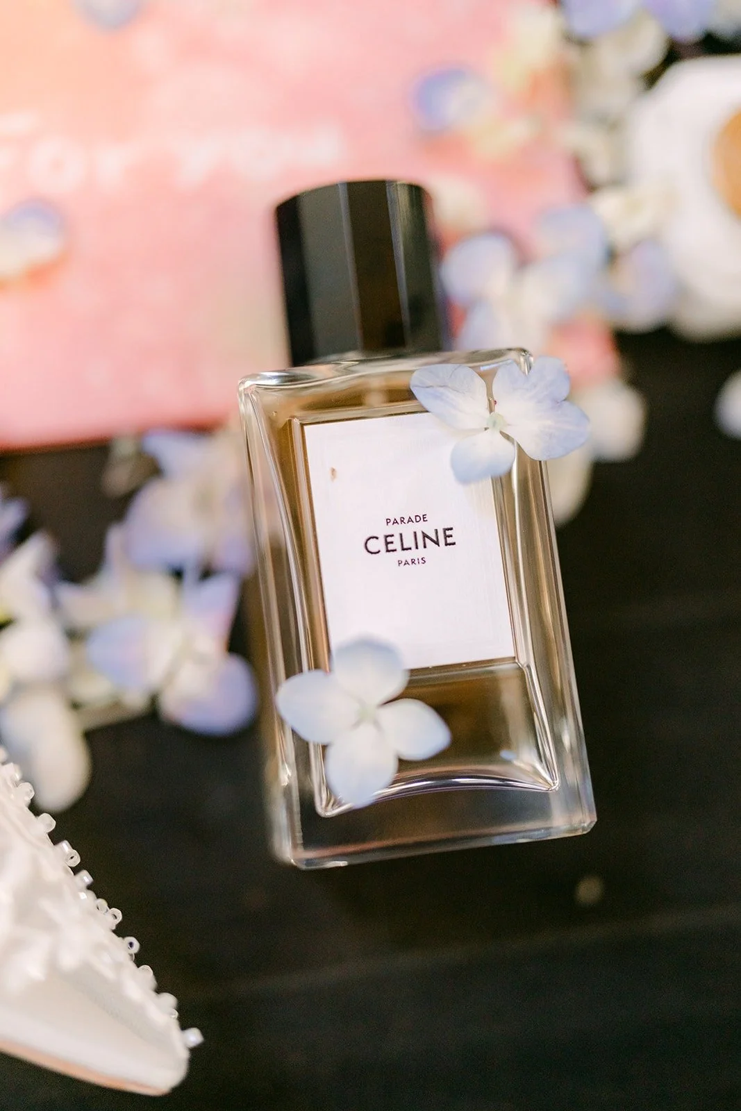 A bottle of perfume resting on blue flowers and blush pink stationery