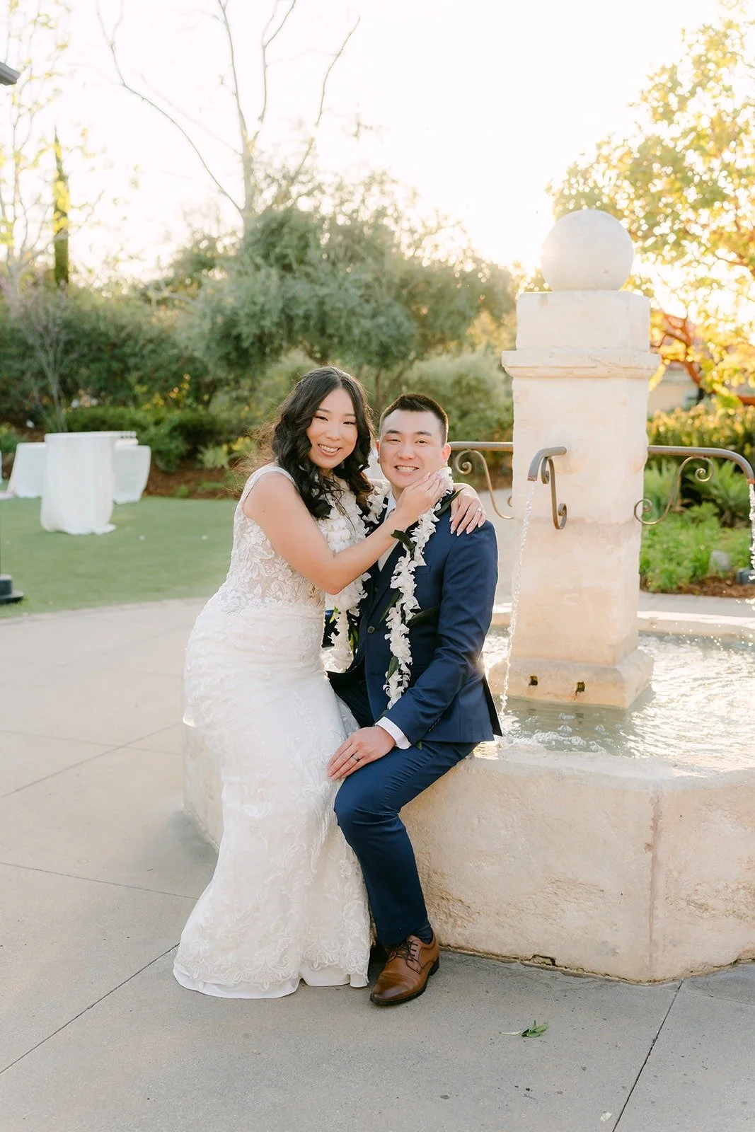 Kelli and Alex sitting on the fountain edge at Los Robles Greens with white leis