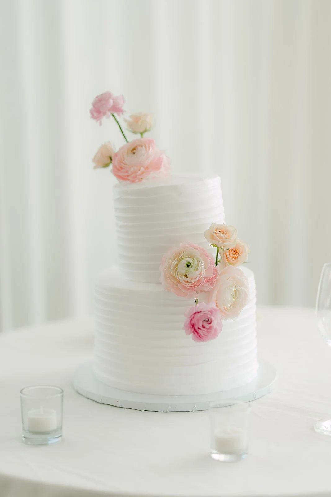 Two-tier white wedding cake topped with blush ranunculus