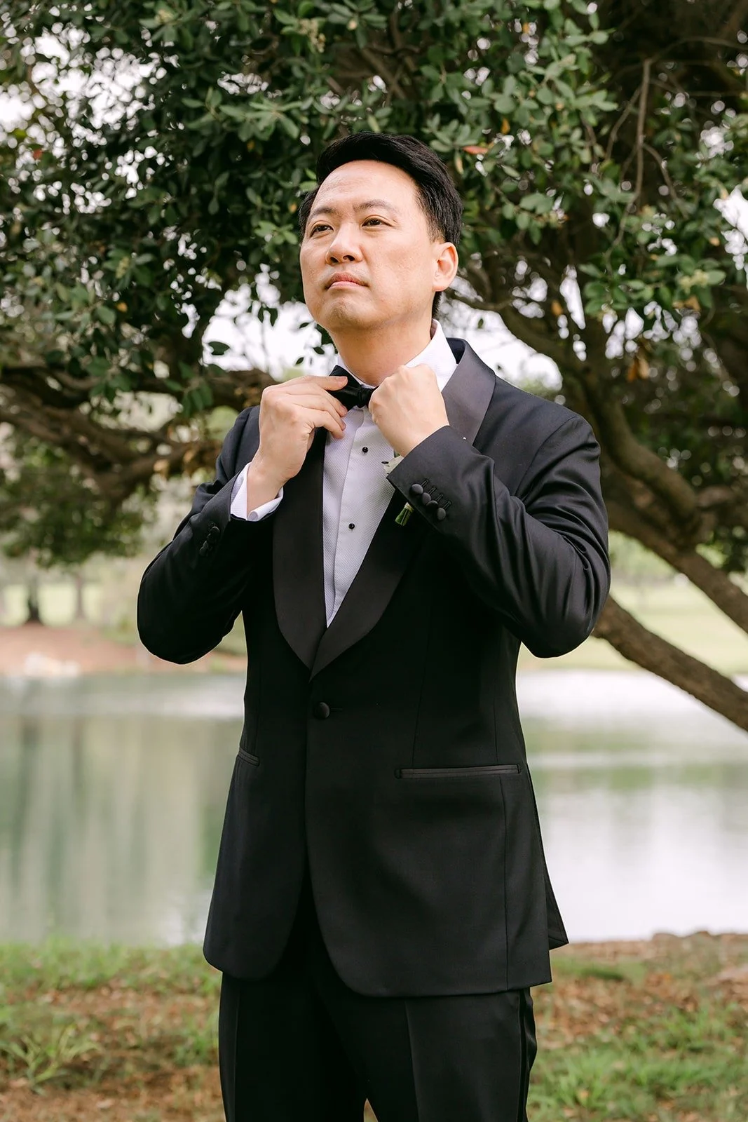 William adjusting his bow tie under the trees by the lake