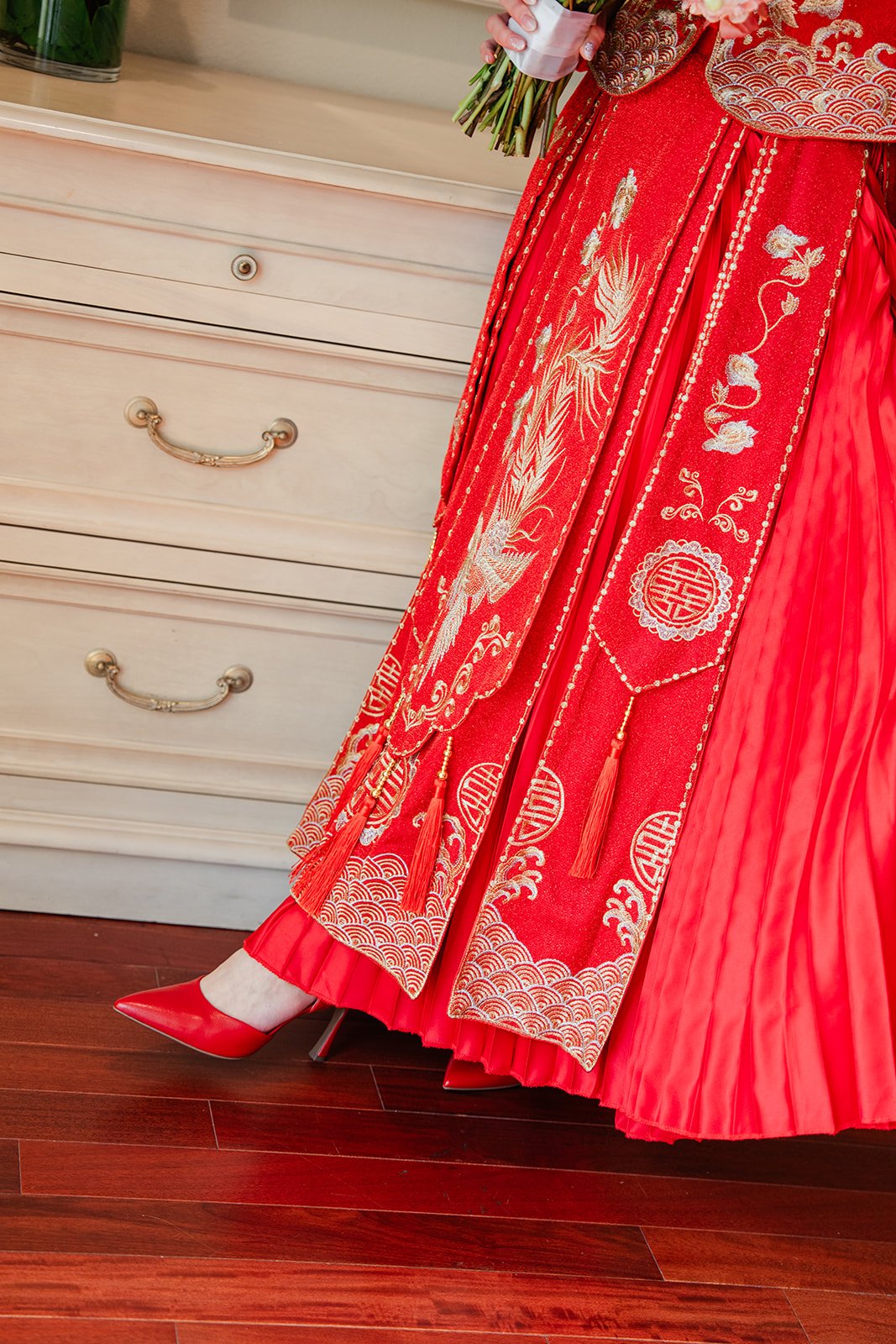 The pleated red skirt of a qun kwa as the bride walks across the room.