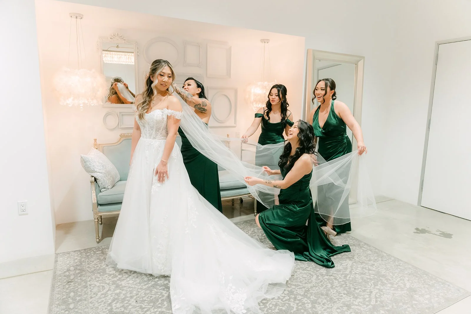 Bridesmaids in emerald satin dresses helping Raine with her gown