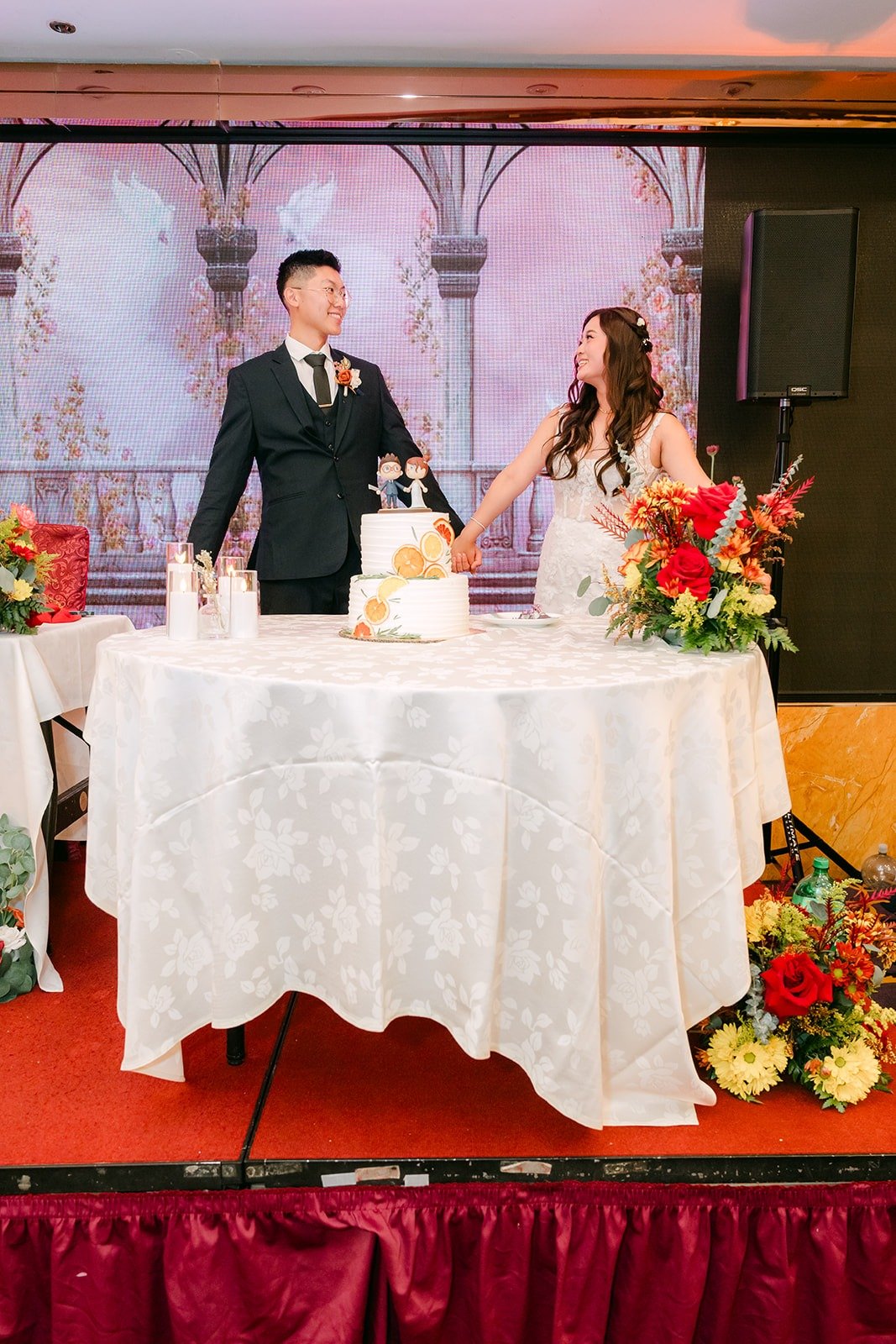 Shayna and Robert stand behind their cake on the stage