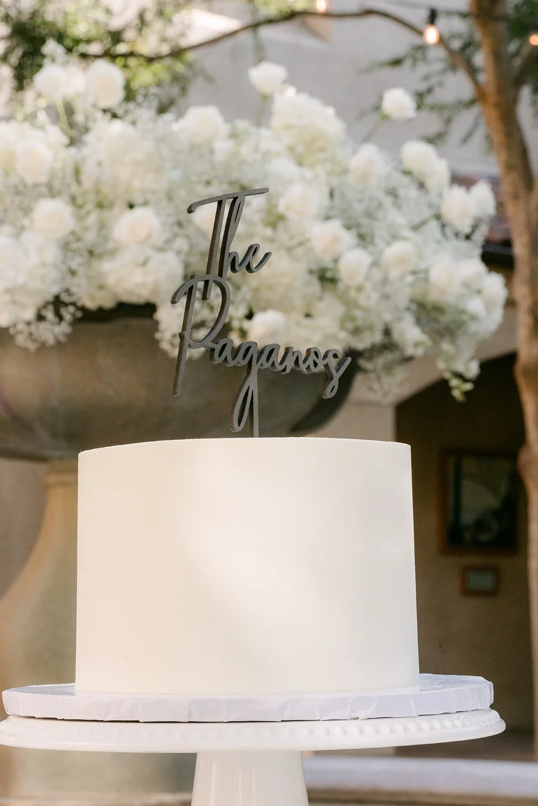 White wedding cake with a gold Paganos topper and white florals