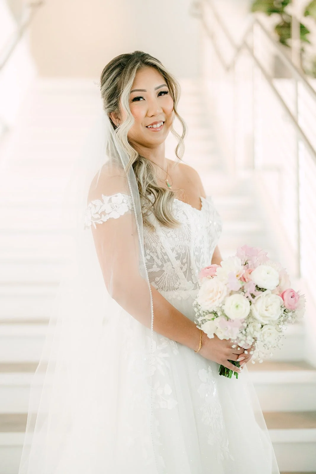 Raine smiling with her bouquet and veil in soft window light