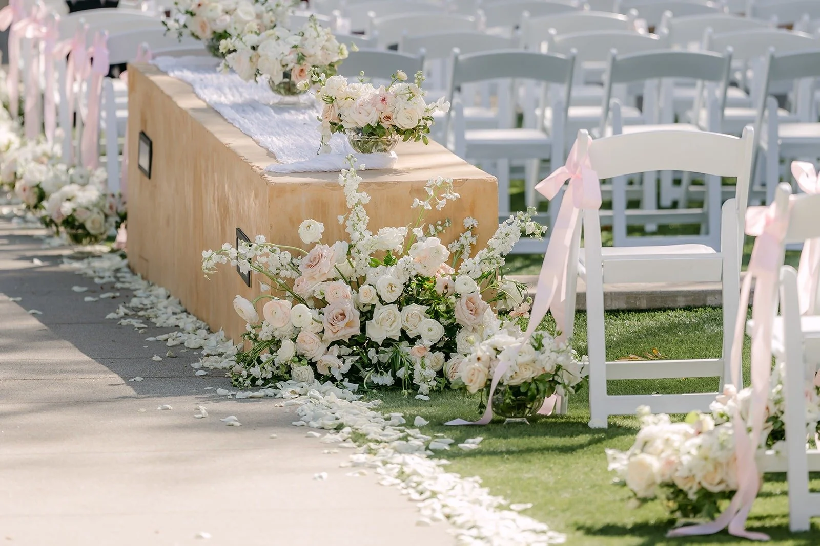 Ivory and blush florals lining the aisle beside white folding chairs