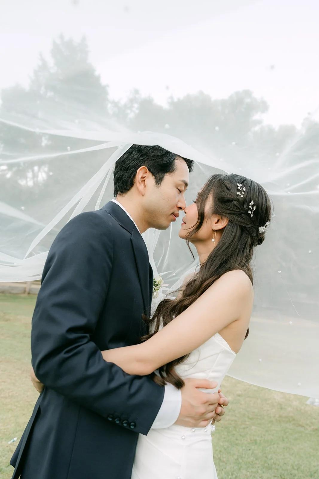 Couple kissing beneath a floating veil at golden hour