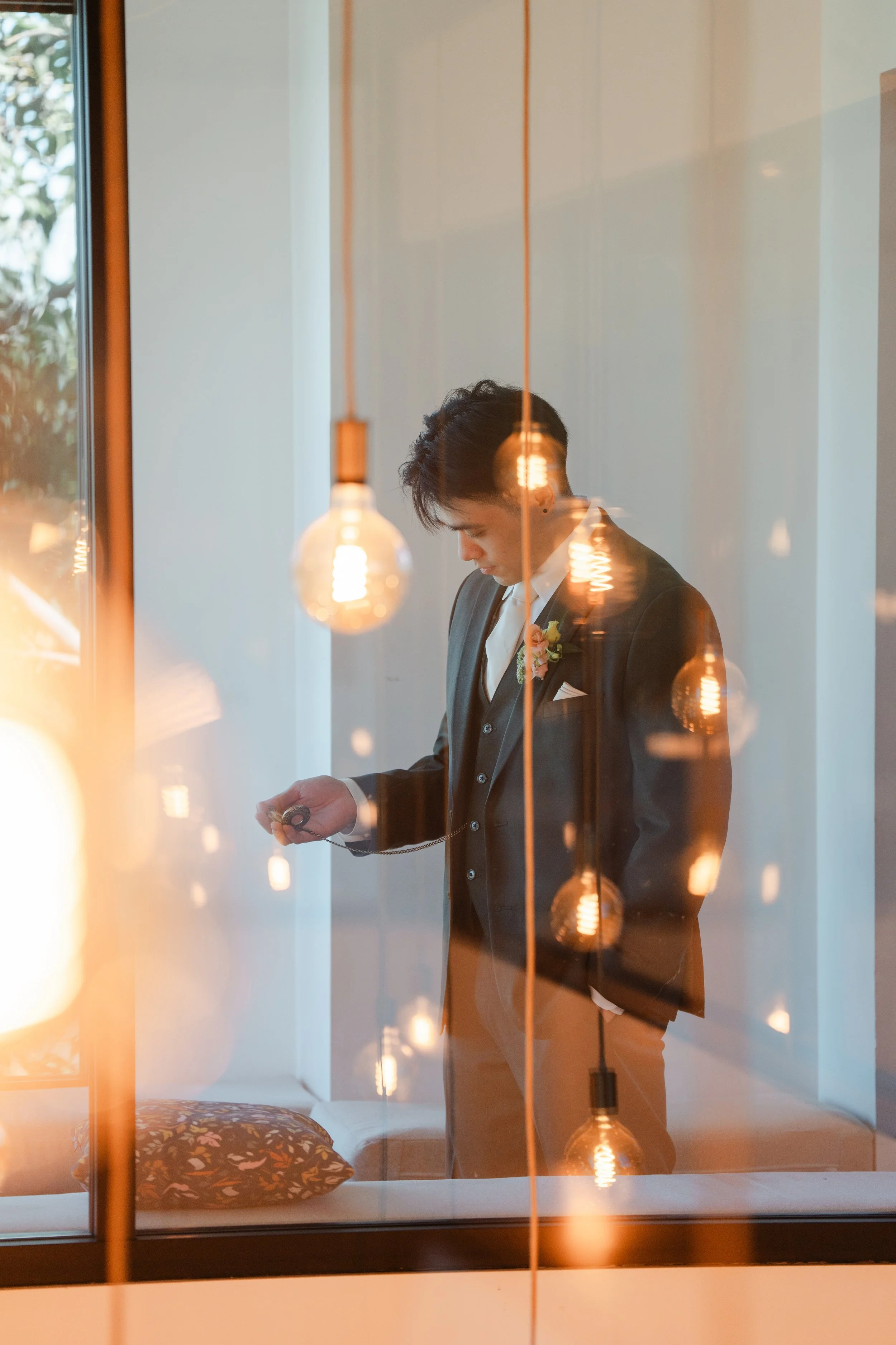 Alex getting ready behind glowing hanging bulbs at The Colony House
