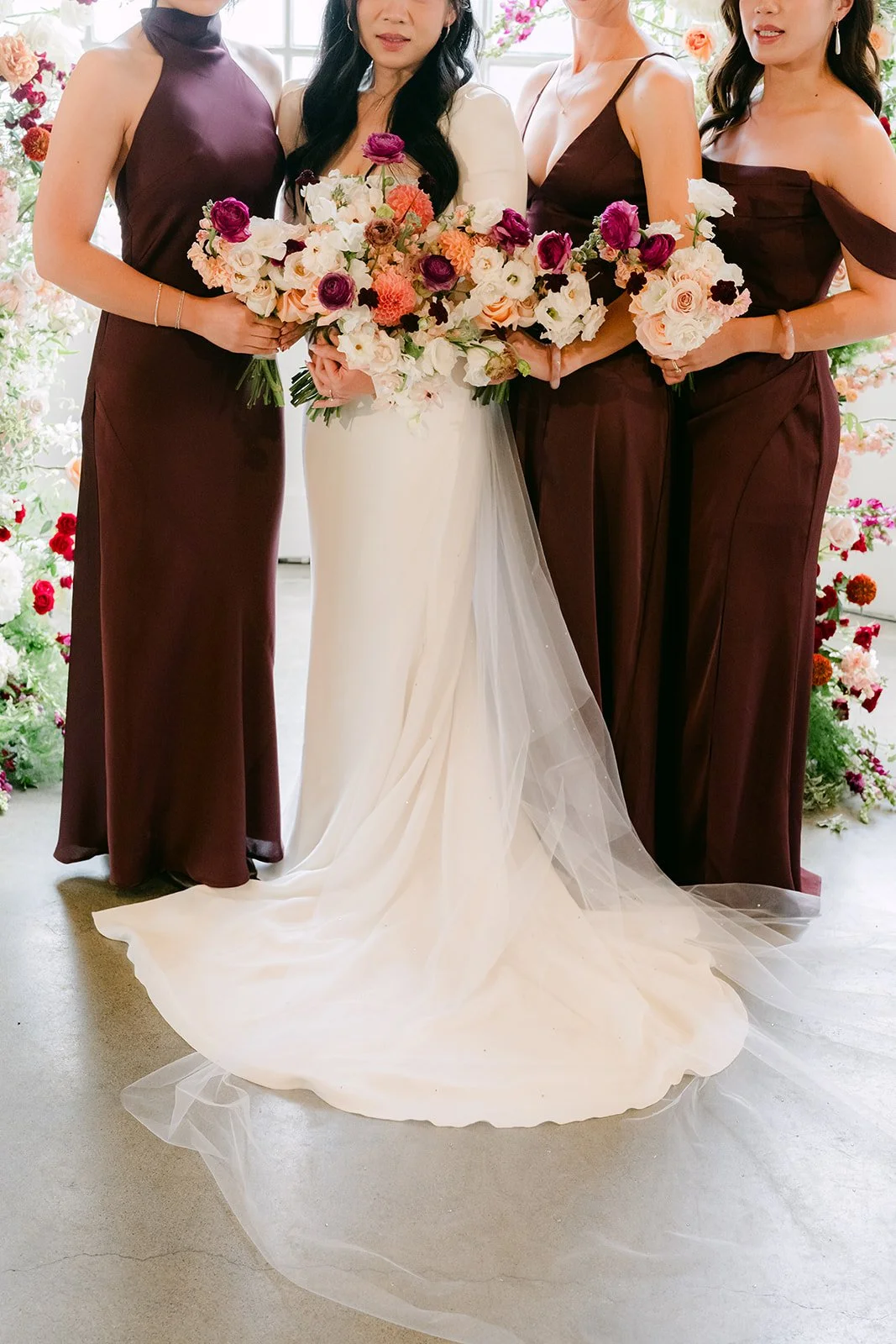 Bridesmaids holding their bouquets around Denise and her train.