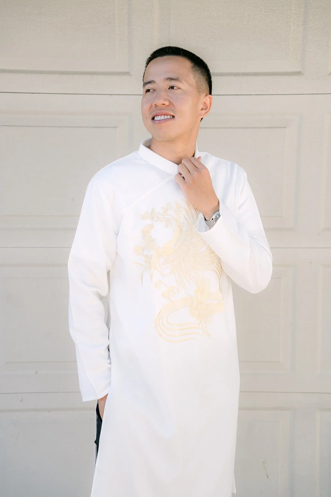 Kevin smiles in his white ao dai with gold embroidery