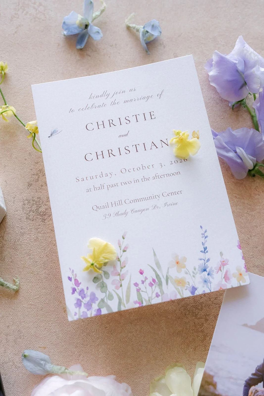 Christie and Christian's wedding invitation surrounded by lilac sweet peas and small flowers.