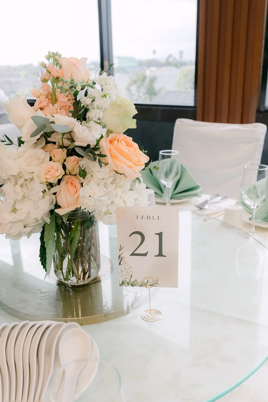 A centerpiece of peach roses and white flowers with a table number