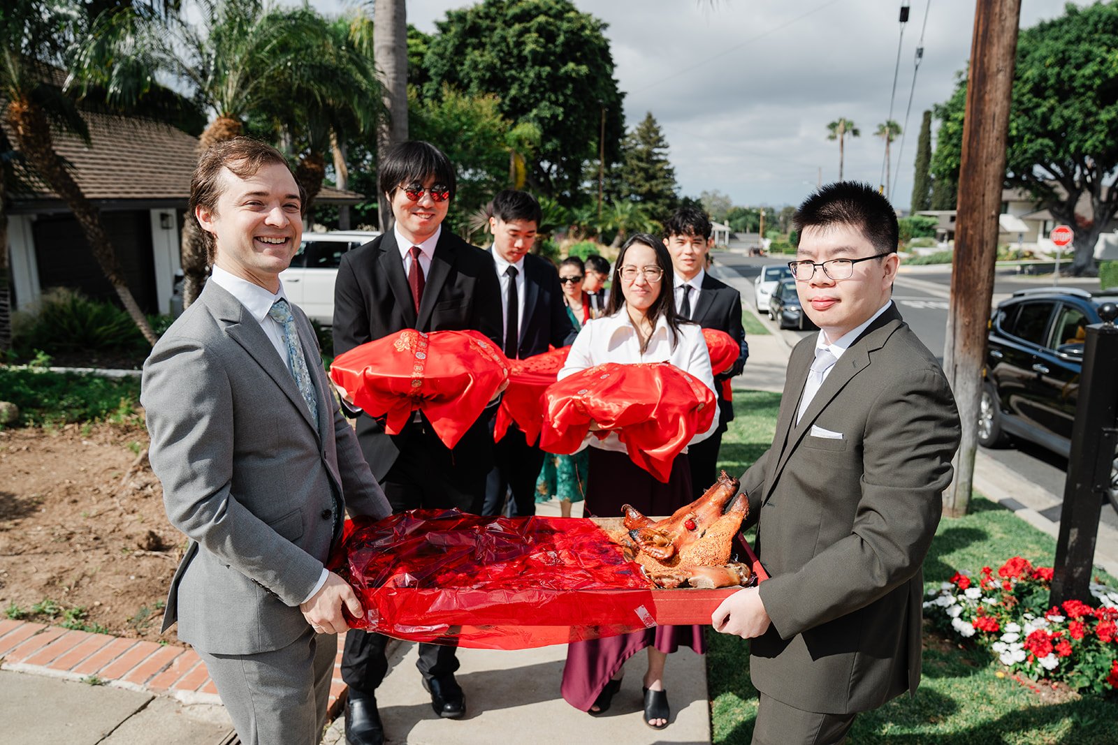 Groomsmen in suits carrying red gift trays toward the bride's home.
