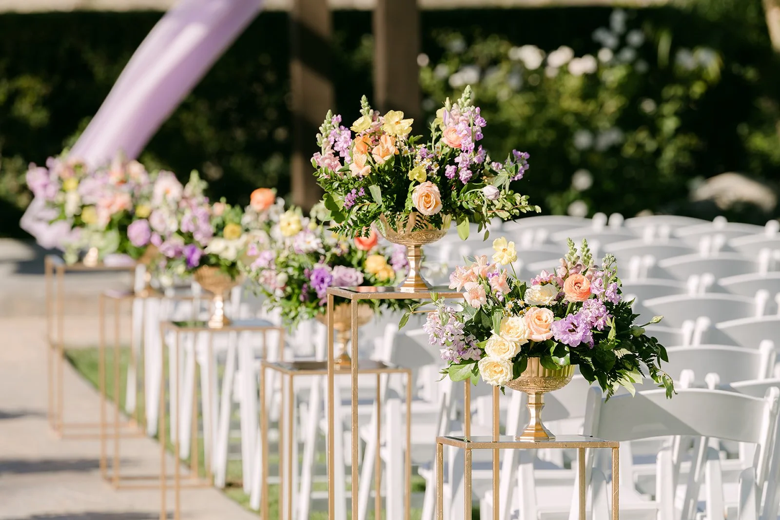 Lilac and peach florals on gold stands lining the aisle.