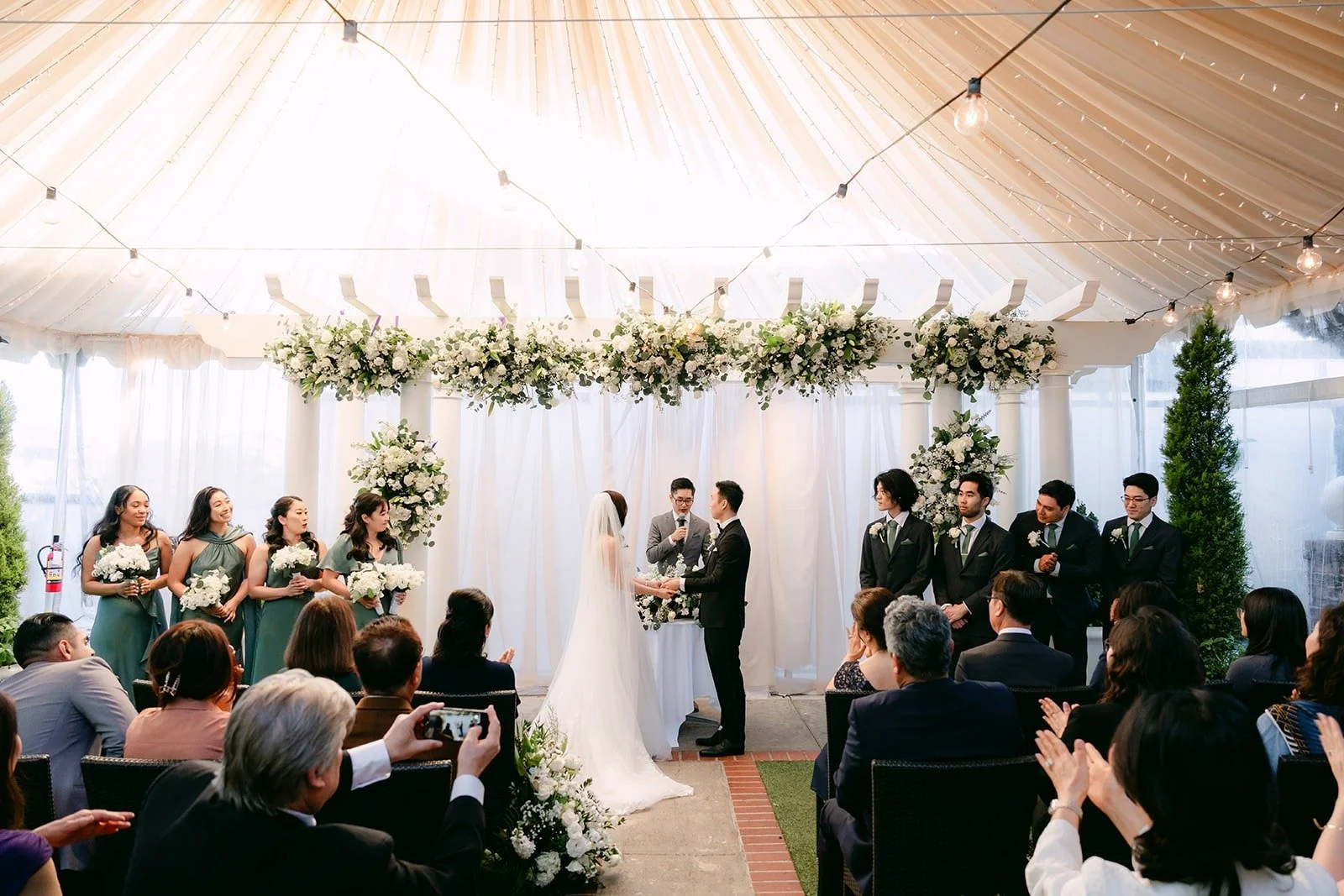 Wide view of the ceremony under the draped canopy and string lights