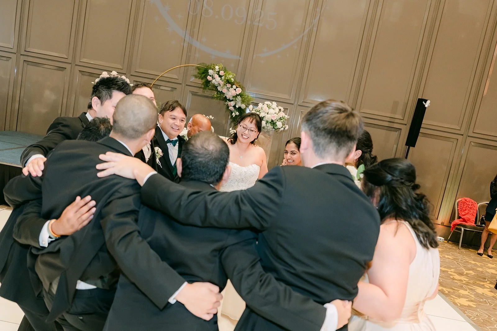 The wedding party wrapping Stella and James in a group hug on the dance floor