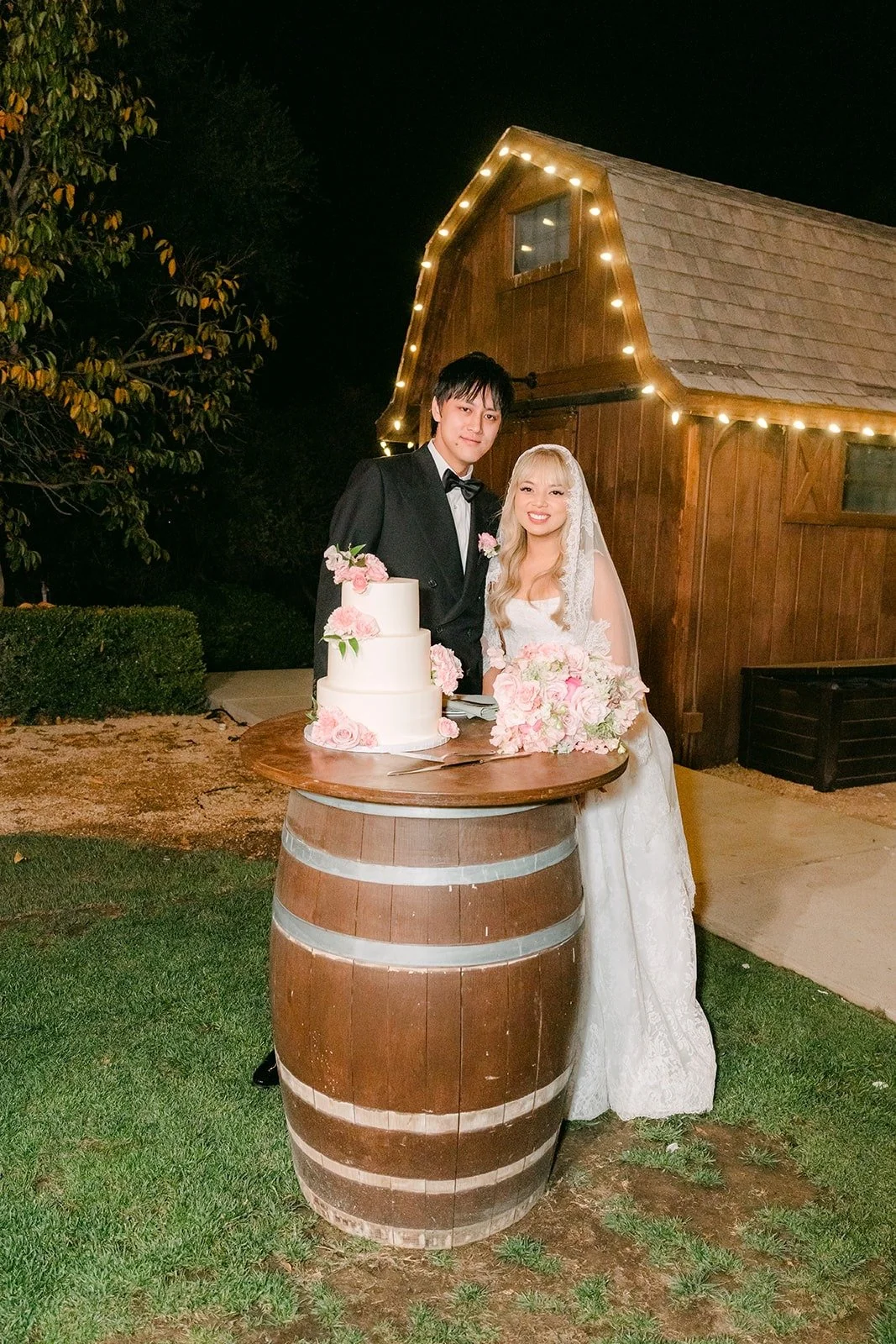 Konitha and Job cutting their cake by the lit barn