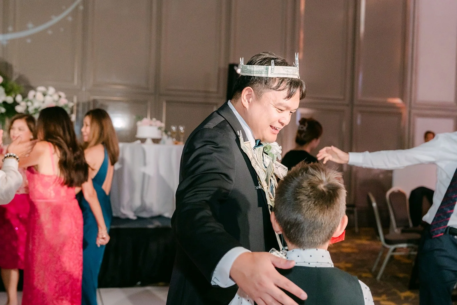 James wearing a crown with bills pinned to his tuxedo during the money dance
