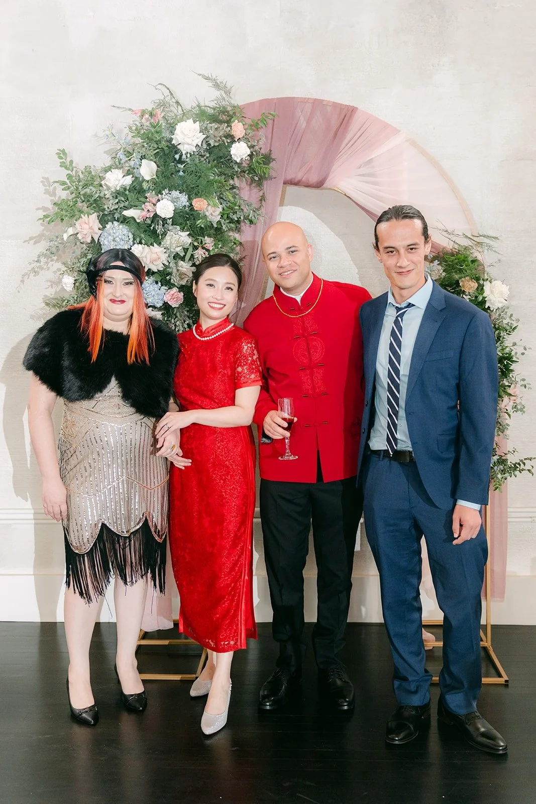 Elisa and Brandon in red with friends at the ceremony arch, photographed by One and Only Production