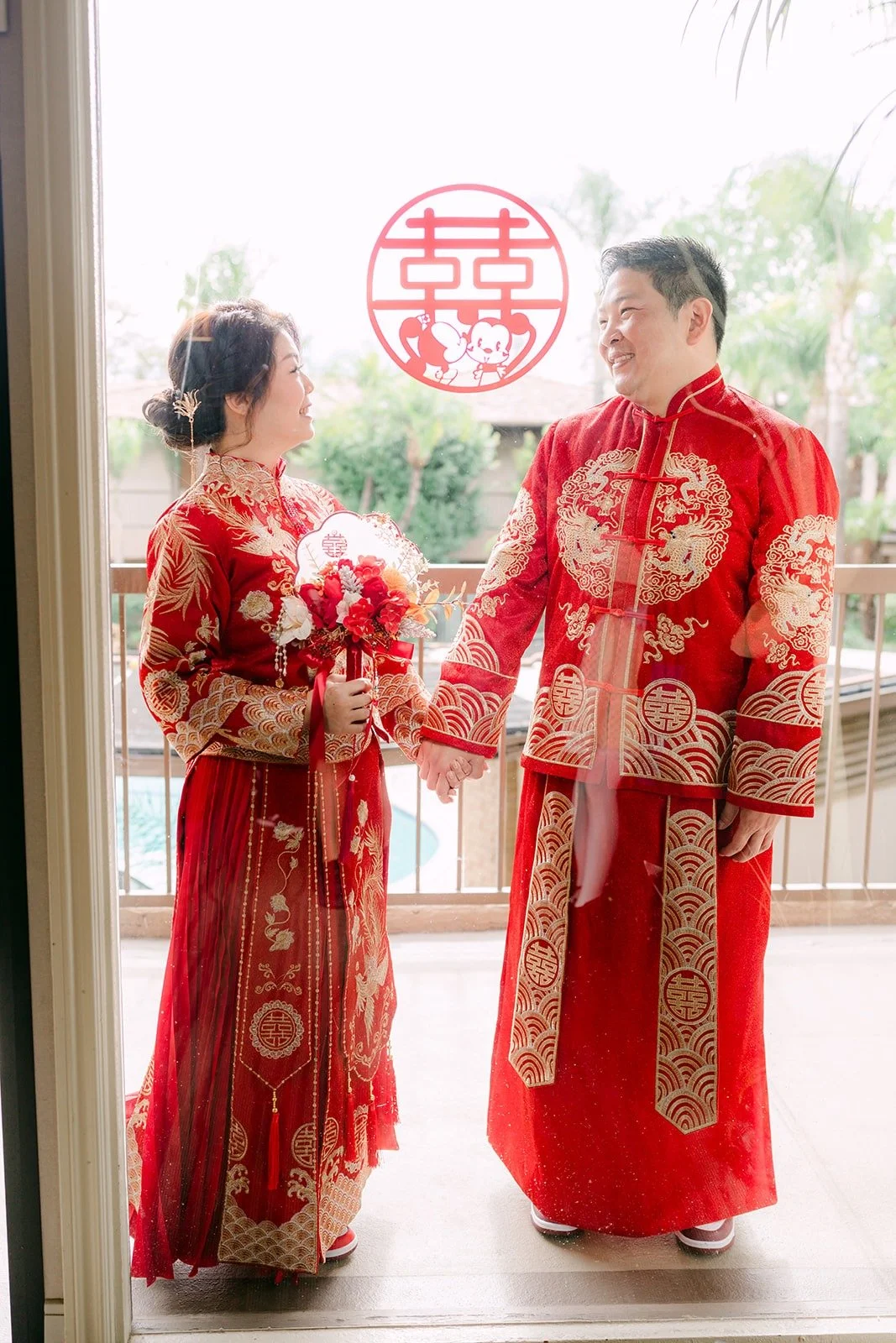 Sochi and Jay hold hands under a red double happiness sign
