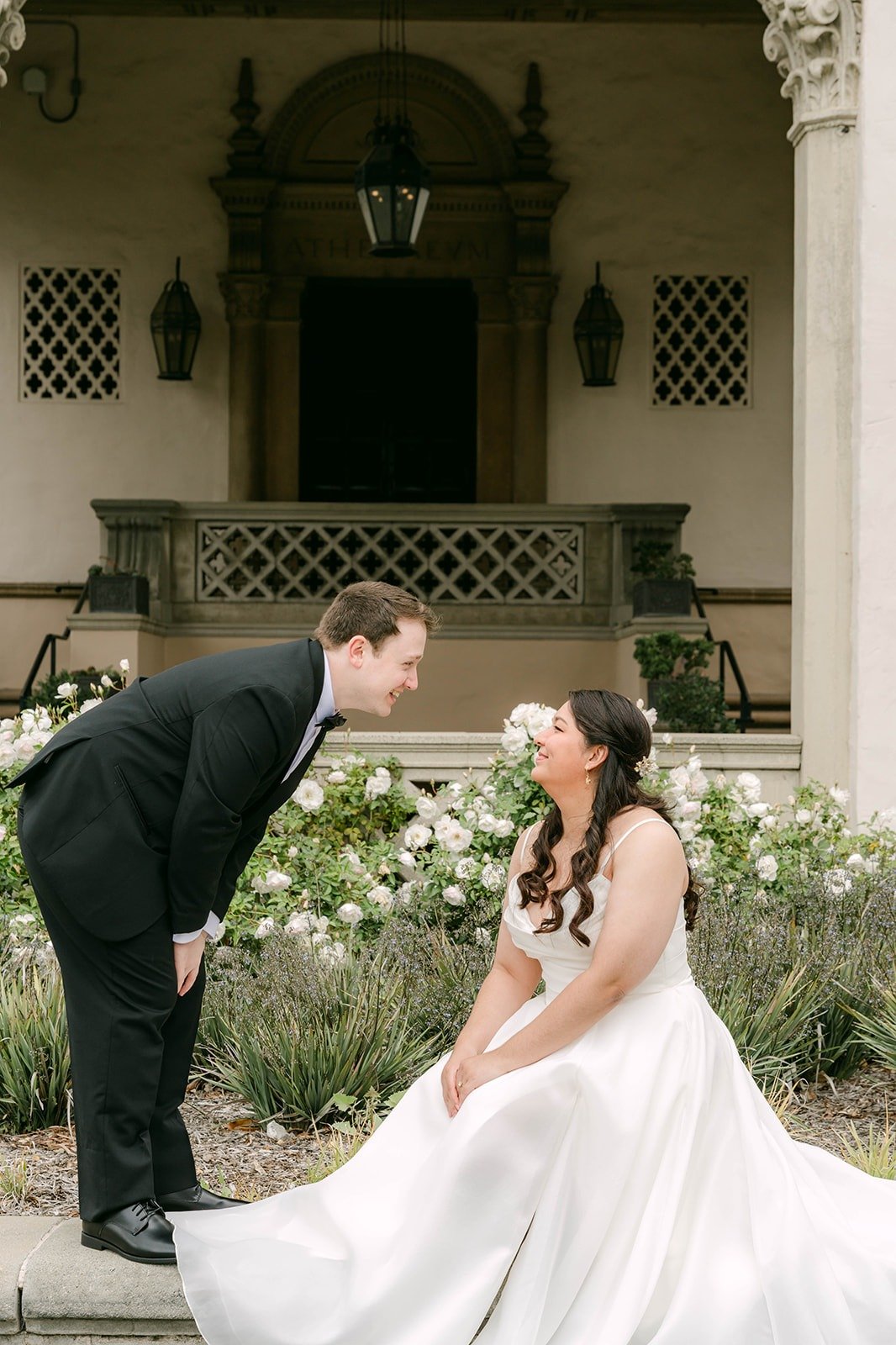 Matthew leaning in toward Saira beside the white roses at the entrance