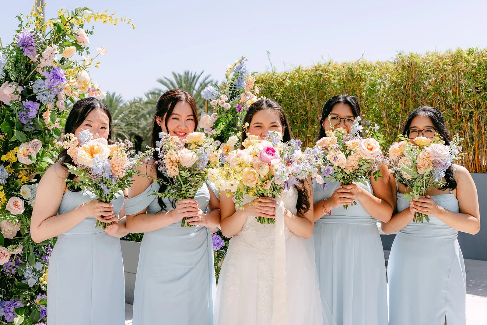 Bridesmaids in light blue hiding behind their bouquets around the bride