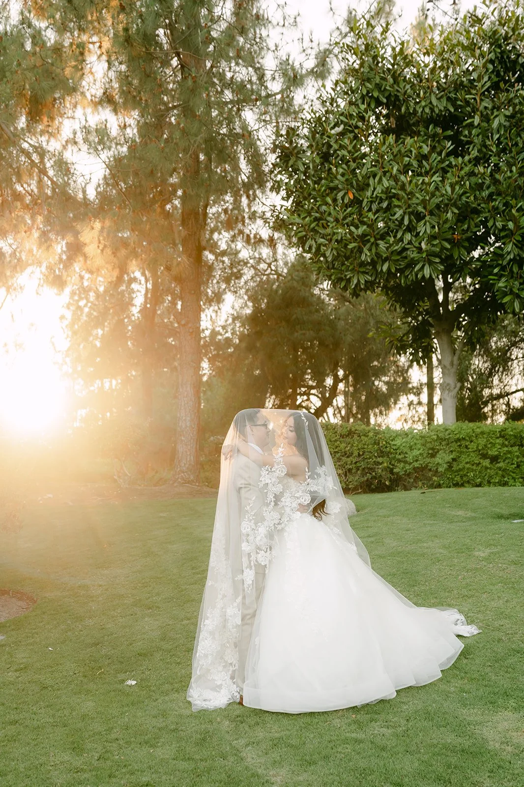 Sandra and Kevin under the veil with the sun setting behind the trees.