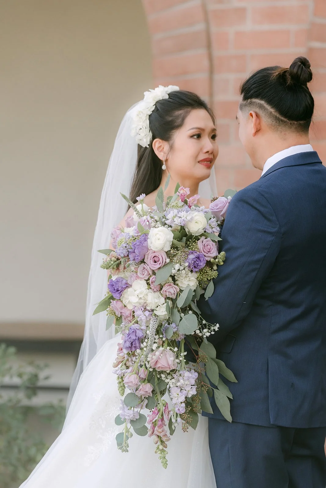 Kate holding her cascading lilac bouquet as Michael looks on.