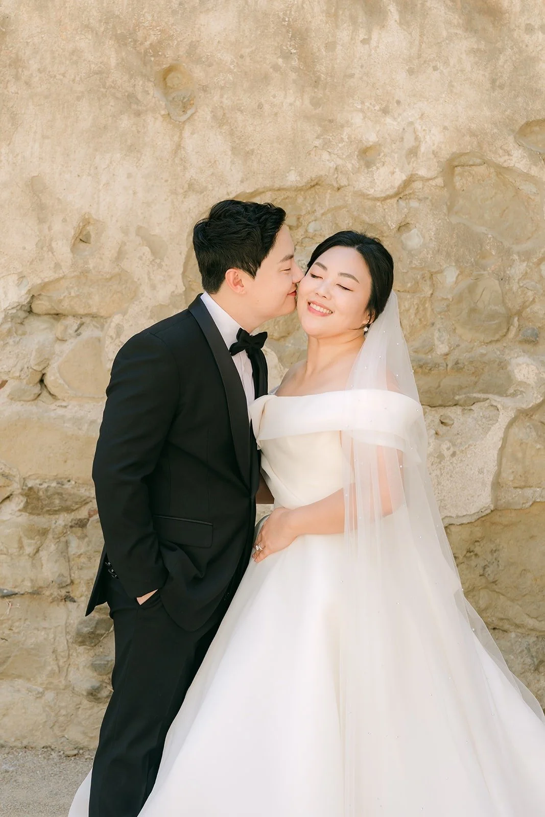 Min Soo kissing Chorok on the cheek against a sunlit stone wall