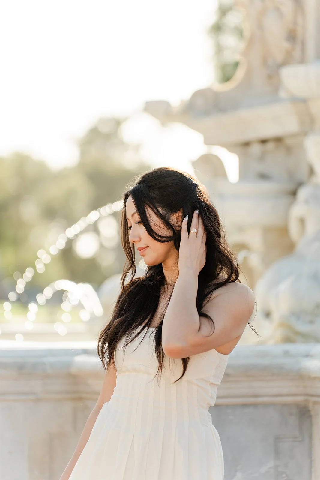 Victoria brushes her hair back in the afternoon light by the fountain.