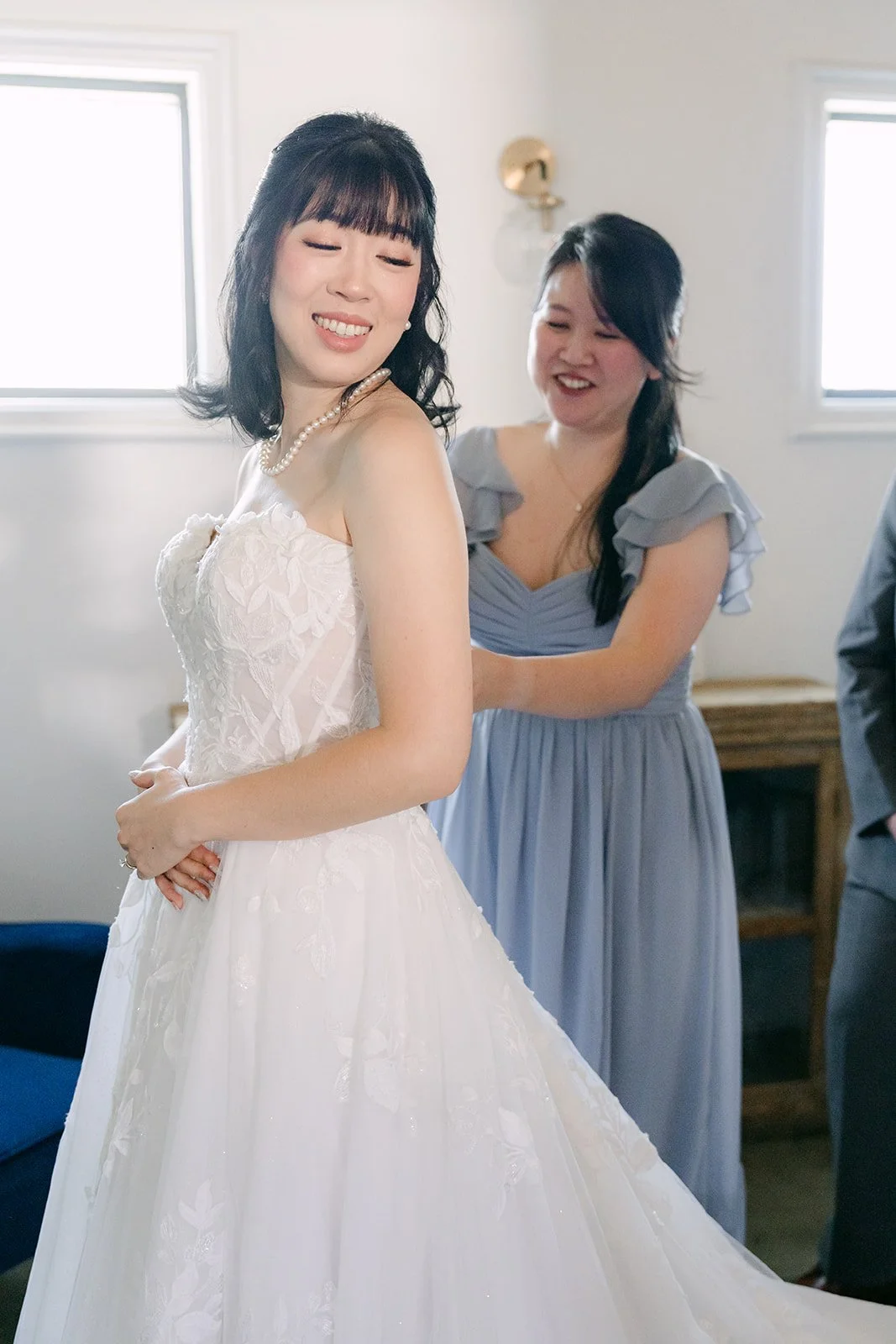 Bridesmaid in dusty blue buttoning Vivian's gown