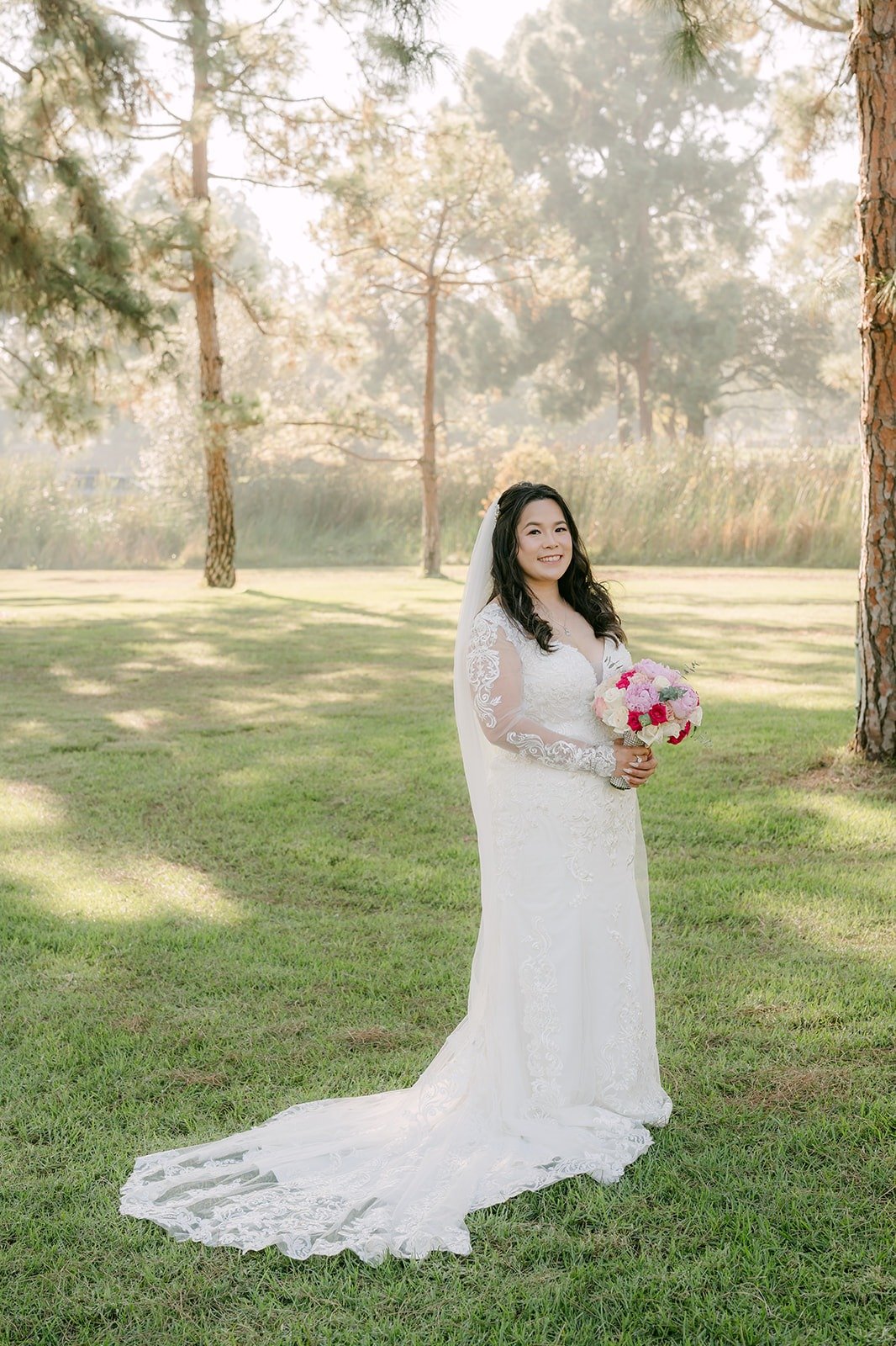 Amy in her lace gown holding a pink bouquet on the lawn at El Dorado Nature Center