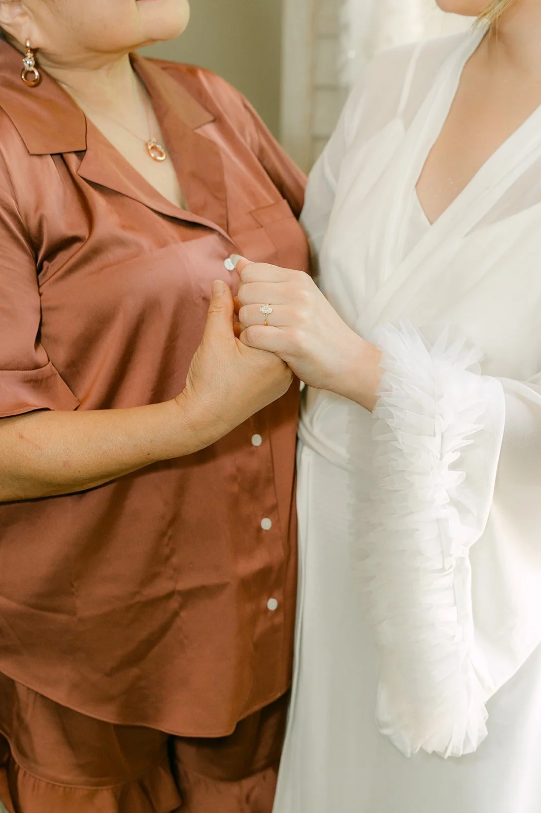 A bridesmaid in a satin pajama set holding Joanne's hand in her white robe