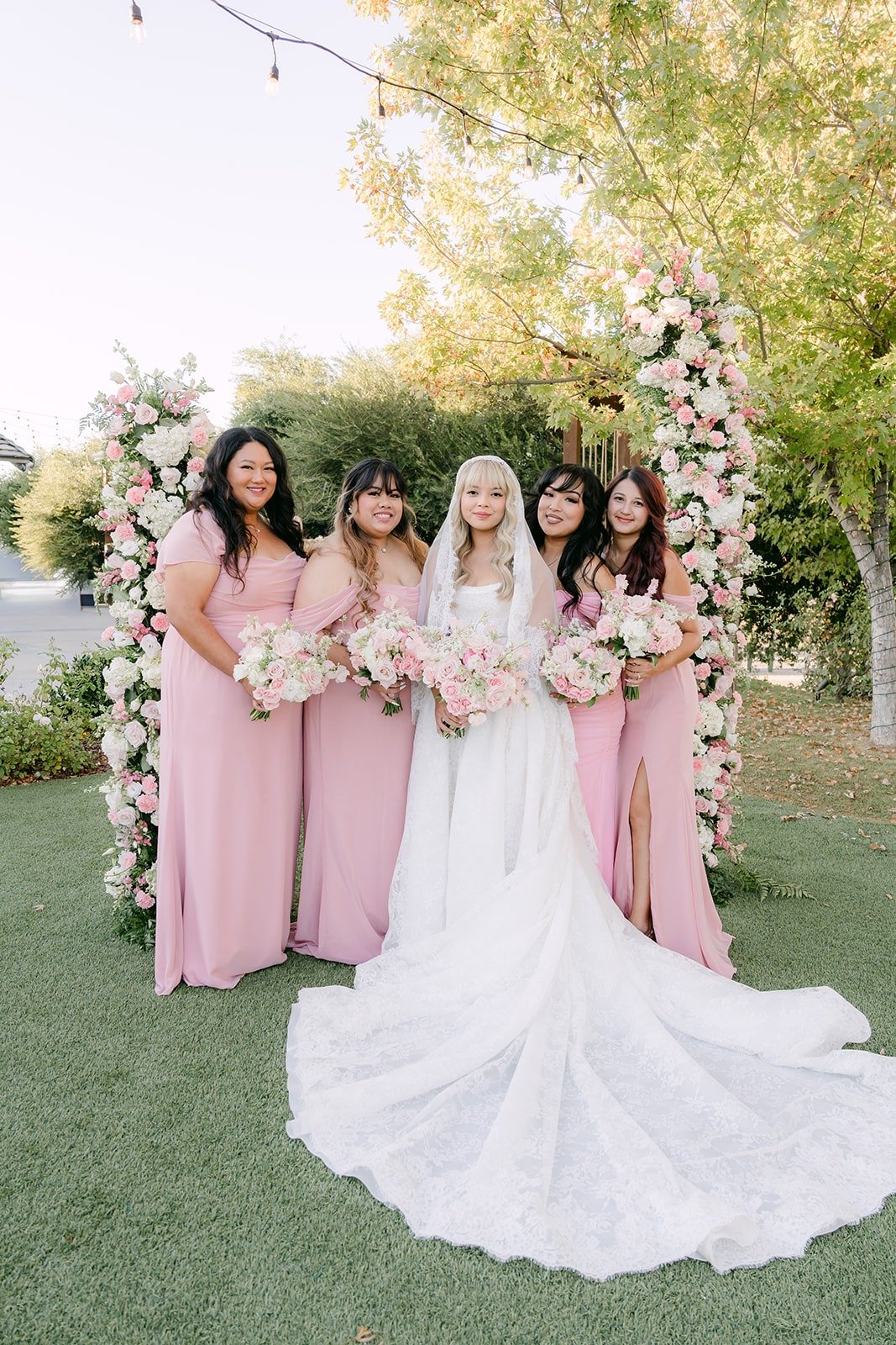 Konitha with her bridesmaids, her long train spread on the lawn