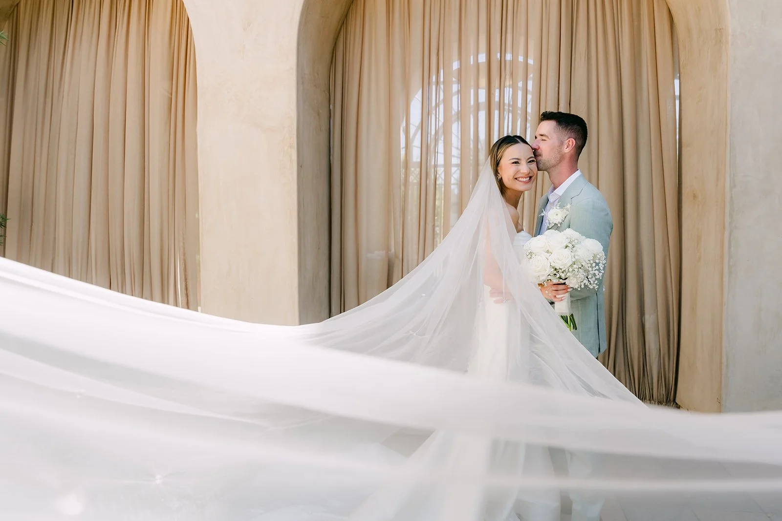 Kieu's long veil flowing across the frame as Anthony kisses her temple