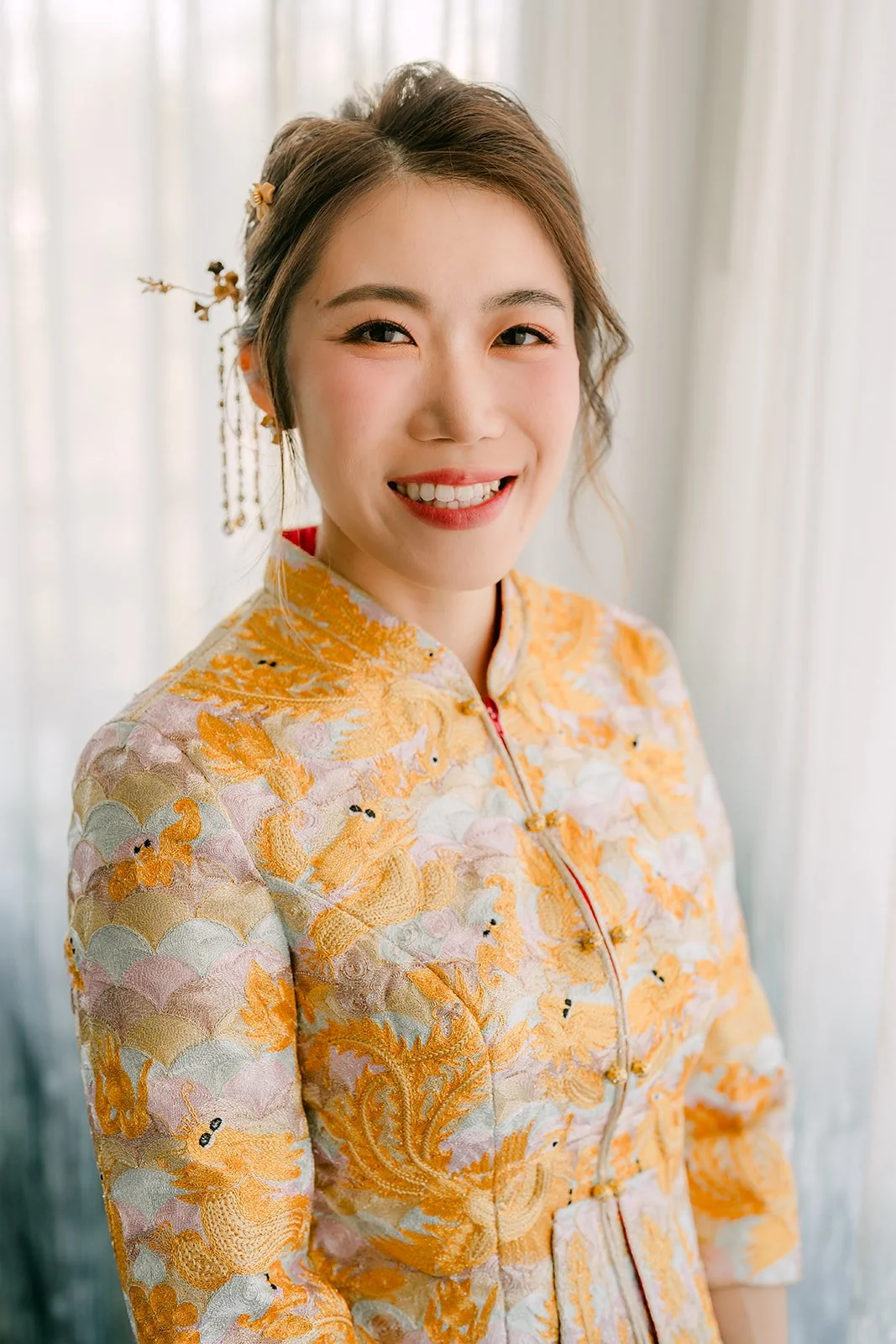 Close portrait of Christie smiling in her gold embroidered qun kwa.
