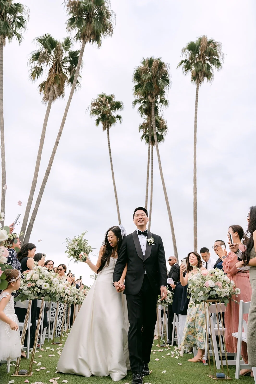 Kristine and William walking up the aisle under the palm trees, photographed by One and Only Production