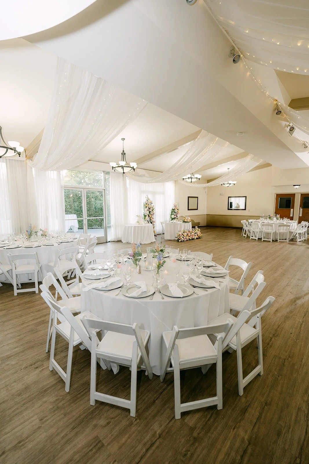 Round tables with white linens and white chairs under draped ceilings