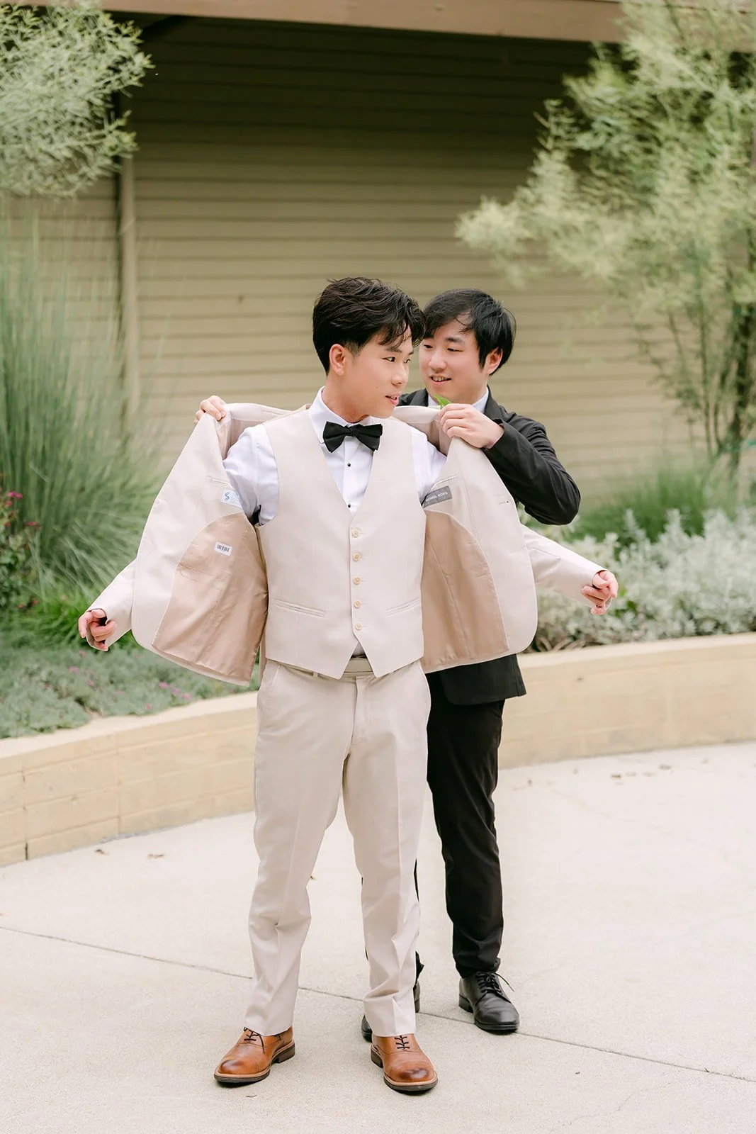 Best man Henry helping Wen into his cream tuxedo jacket.