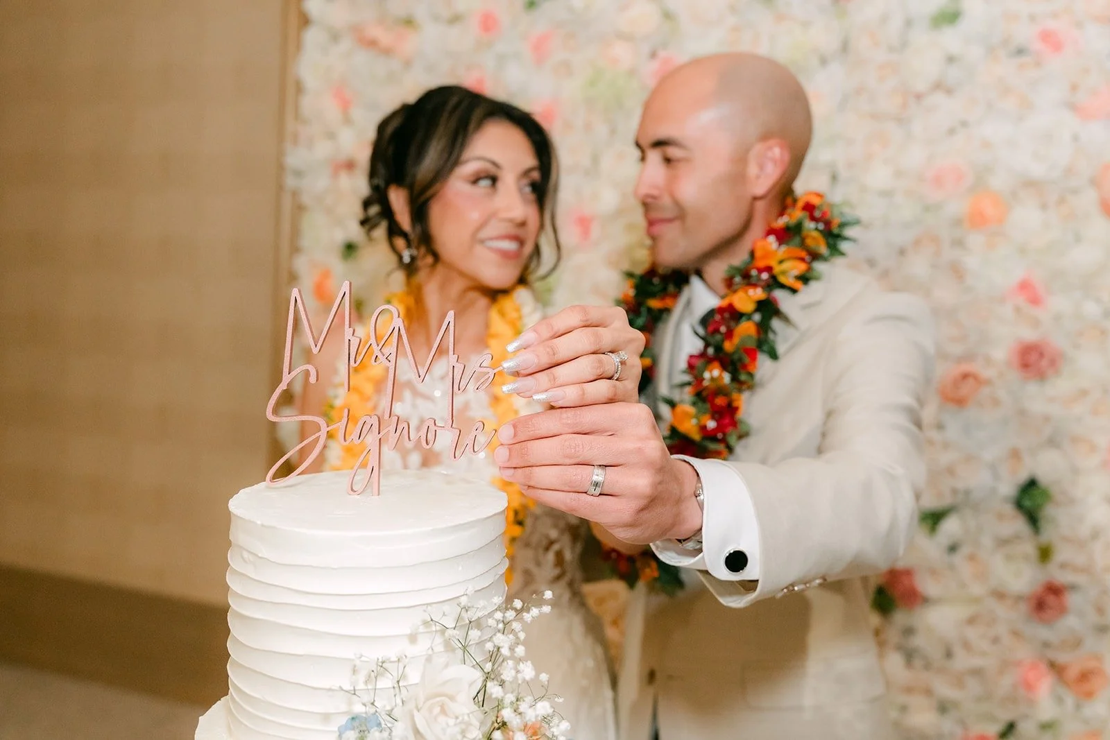 Francesca and Daniel in flower leis cut their wedding cake