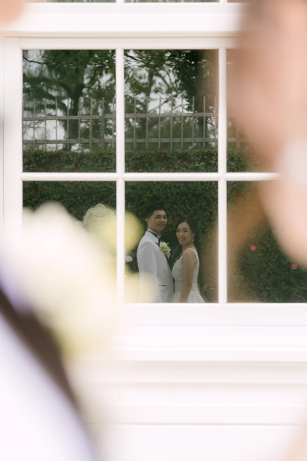 Jenny and Ryan framed through a window with florals in the foreground, photographed by One and Only Production.