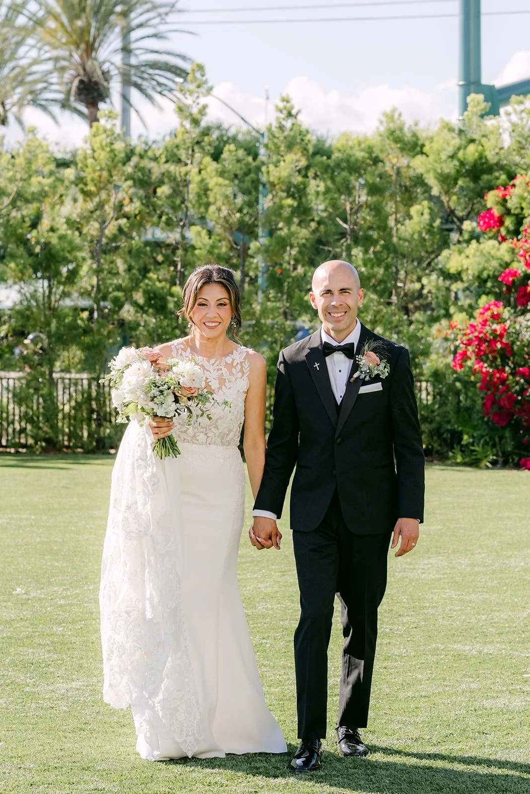 Francesca and Daniel walk hand in hand past the garden hedges