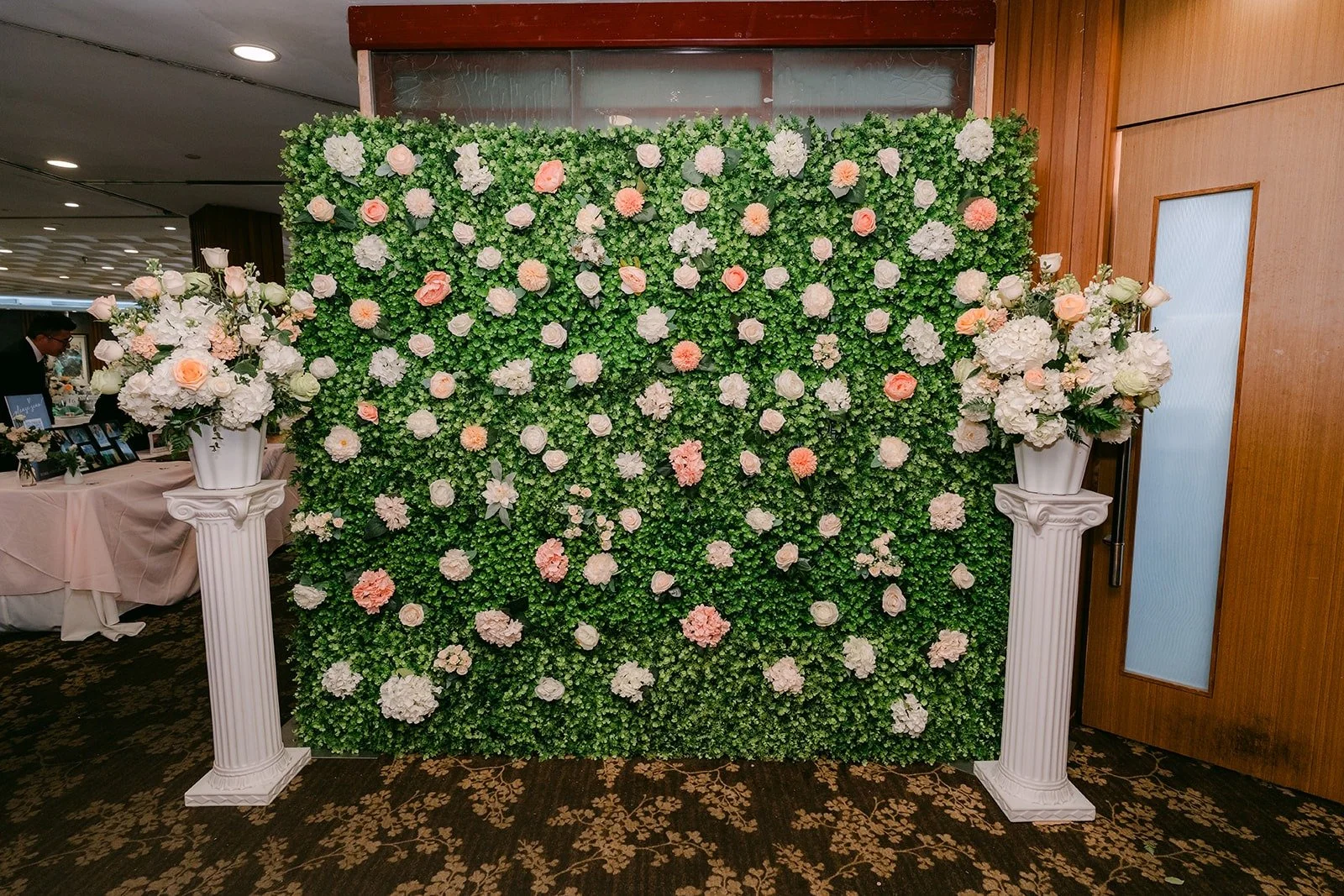 A flower wall of greenery with white and blush roses for guest photos, photographed by One and Only Production