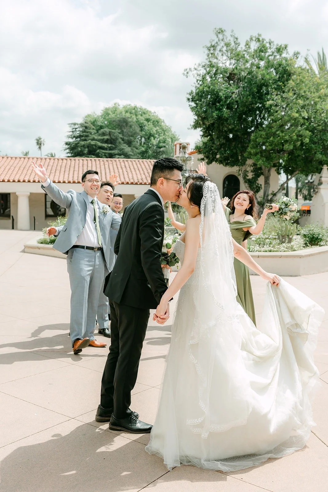 The wedding party cheers as Eunice and Eric share a moment on the plaza, photographed by One and Only Production