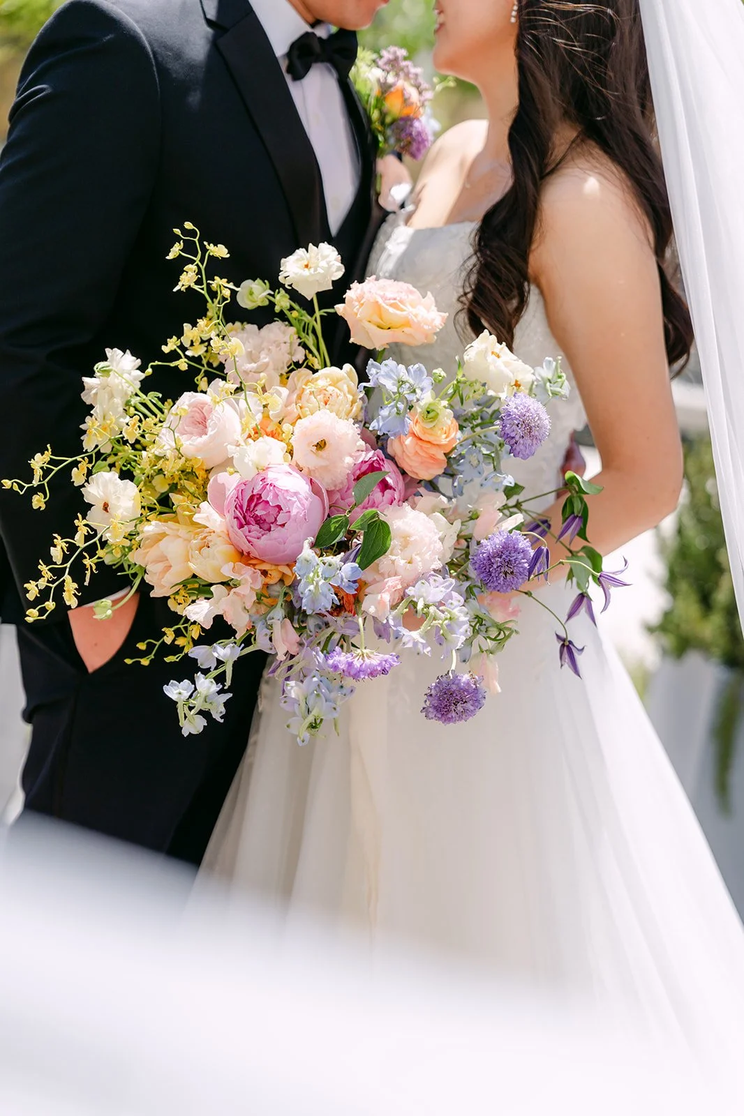 Close up of the bride's pastel rainbow bouquet against the groom's black tuxedo