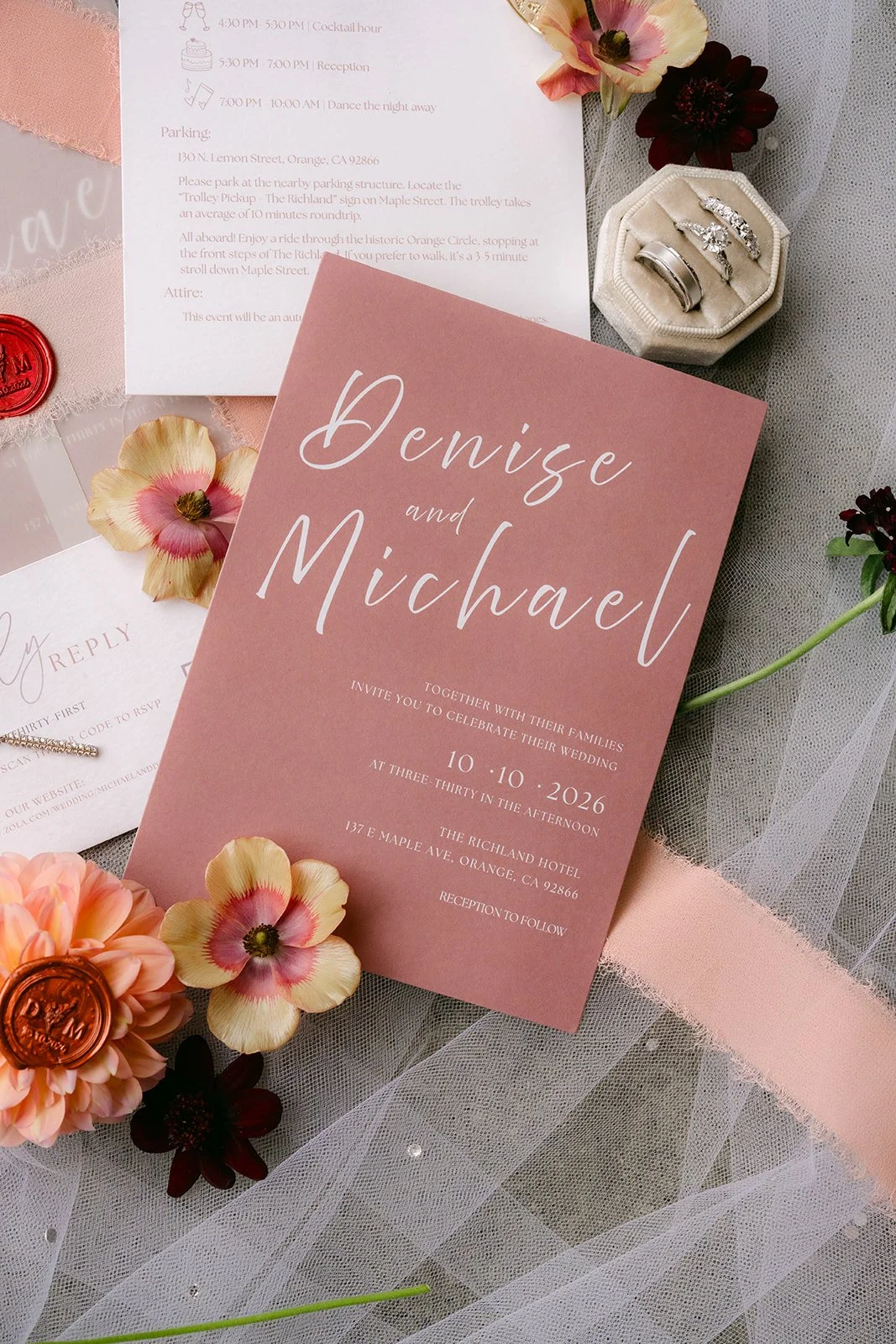 Blush wedding invitation reading Denise and Michael, styled with peach dahlias and burgundy blooms.