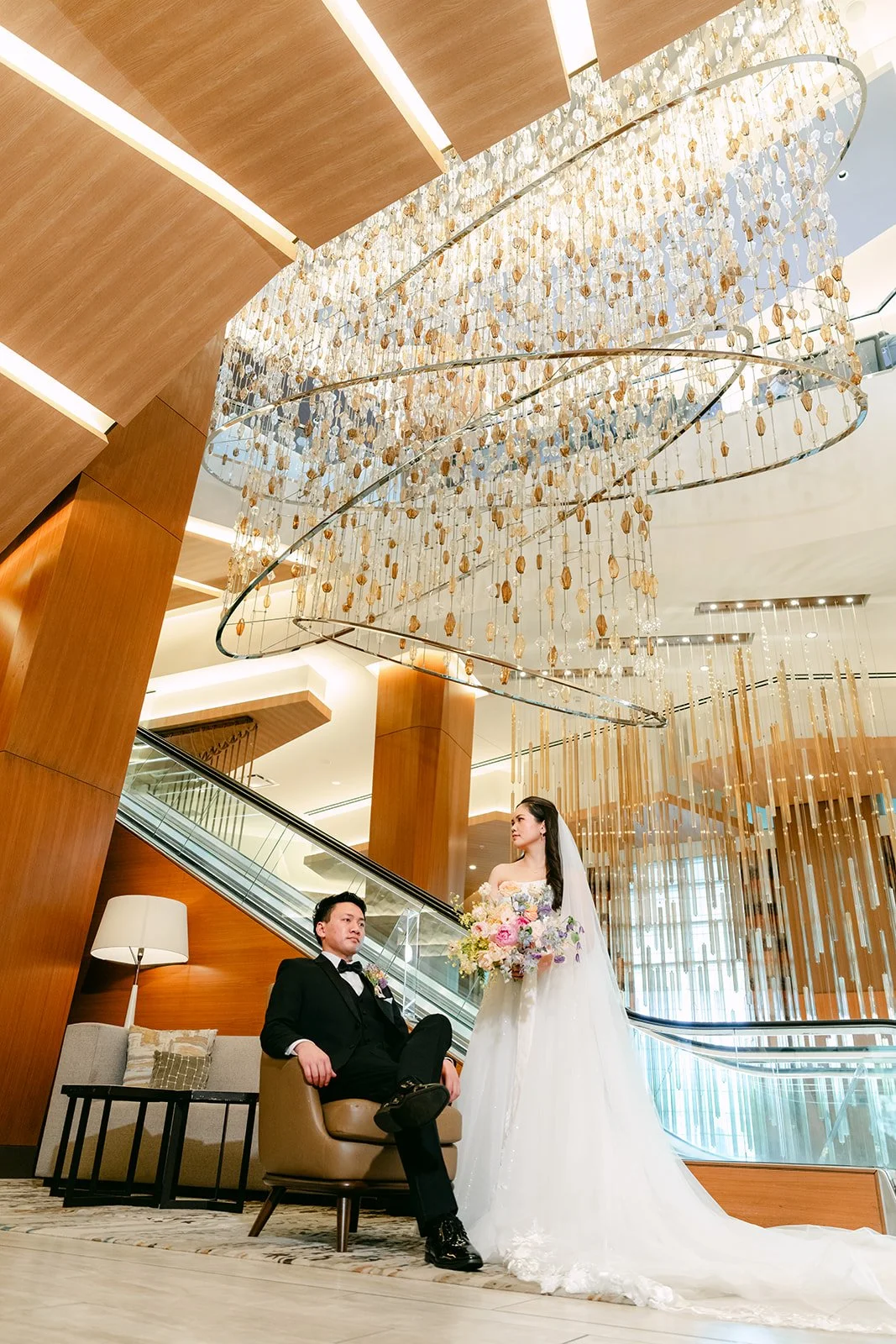Couple seated beneath the grand staircase and chandelier in the JW Marriott Anaheim lobby
