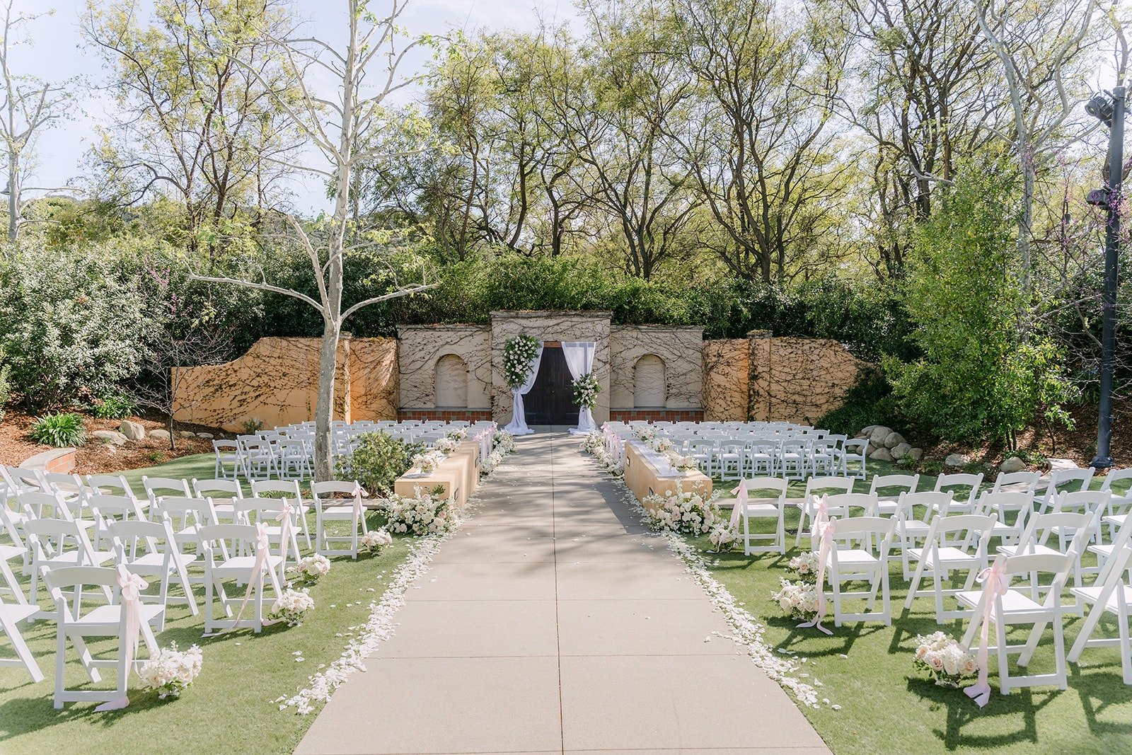 White chairs lining the aisle to the floral arch at the Los Robles Greens ceremony site