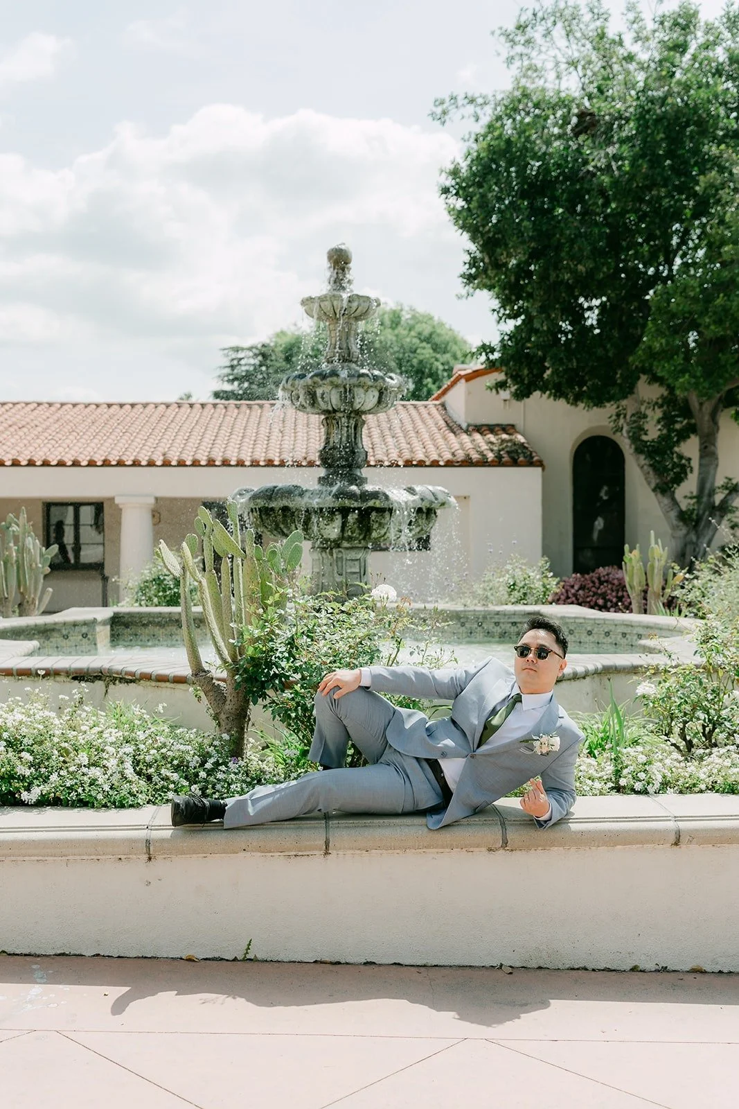 A groomsman lounges on the fountain ledge while the others laugh, photographed by One and Only Production